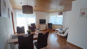 A modern living room with a wooden ceiling, a dining area with a table and chairs, a TV, and a sofa. - Apartment in the countryside (Beilstein)