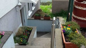 A narrow stairway leading to a building entrance, flanked by flower planters and a metal railing. - Apartment in the countryside (Beilstein)