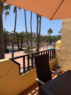 Un balcone con vista su una zona piscina, palme e una montagna sullo sfondo.