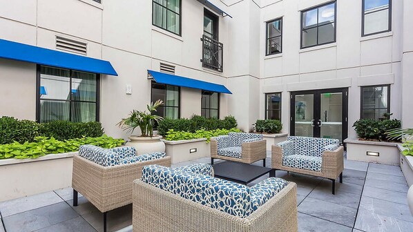 A courtyard with wicker furniture and a black table, surrounded by greenery and a building with blue awnings. - King Street Boutique Resort (Charleston)