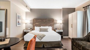 Ein Hotelzimmer mit einem großen Bett, zwei Nachttischen mit Lampen, einem Kleiderschrank und einem kleinen Tisch mit einem Stuhl.