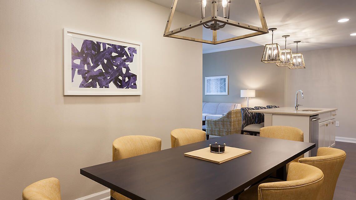 Un comedor moderno con una mesa de madera oscura, sillas color beige y una lámpara colgante contemporánea.