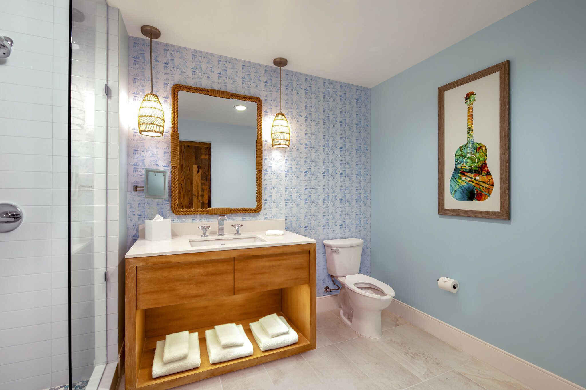 Un baño con tocador de madera, inodoro blanco y espejo con una obra de arte de una guitarra.