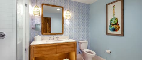 Un baño con tocador de madera, inodoro blanco y espejo con una obra de arte de una guitarra.
