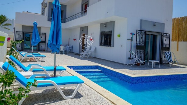 A modern hotel with a swimming pool, sun loungers, and a covered outdoor area. - Adorable villa with pool (Djerba)