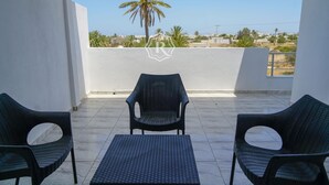 A balcony with two wicker chairs and a small table, overlooking a residential area with palm trees and houses. - Adorable villa with pool (Djerba)