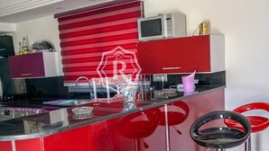 A modern kitchen with a red island, stainless steel bar stools, and a microwave. - Adorable villa with pool (Djerba)