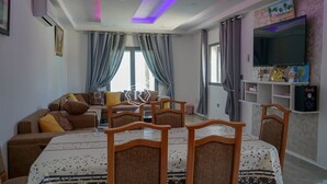 A modern living room with a sofa, dining table, chairs, and a flat-screen TV. - Adorable villa with pool (Djerba)