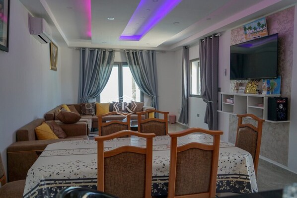 A modern living room with a sofa, dining table, chairs, and a flat-screen TV.