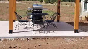 Un área de estar al aire libre techada con una parrilla, sillas de metal y una mesa.