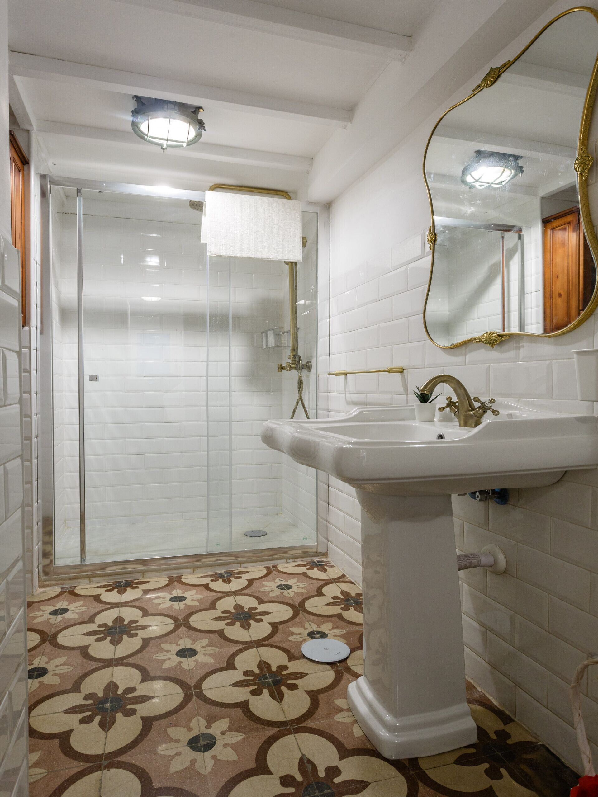 Un baño con lavamanos blanco, un espejo y zona de ducha.