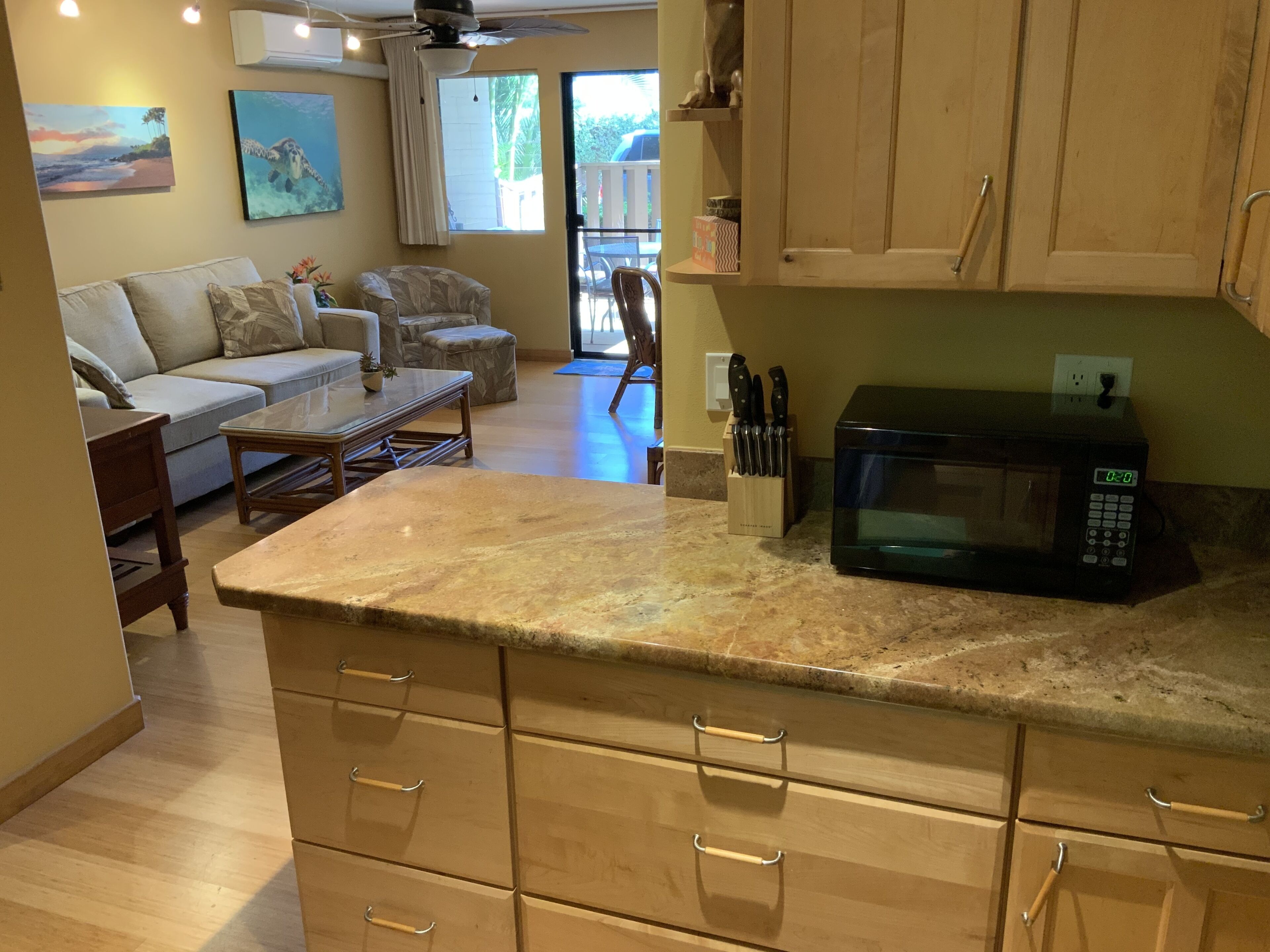 A kitchen with wooden cabinets, a microwave, and a dining area with a sofa and coffee table.