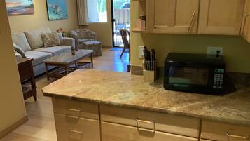 A kitchen with wooden cabinets, a microwave, and a dining area with a sofa and coffee table.