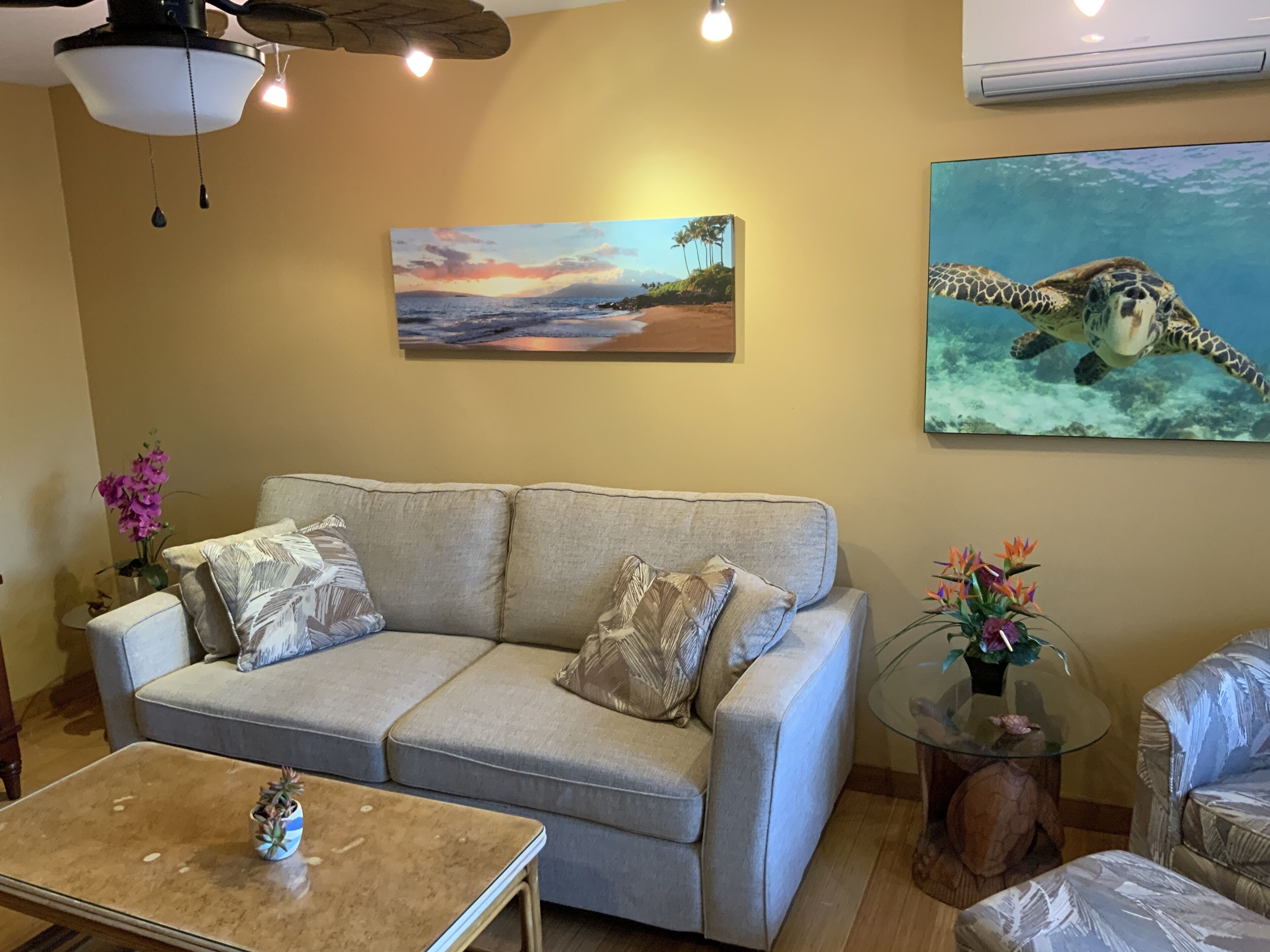 Un salon comprenant un canapé, une table basse, un tableau représentant une plage et un tableau représentant une tortue de mer.