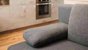 Une cuisine moderne avec des meubles en bois, un four encastré et un canapé gris au premier plan.