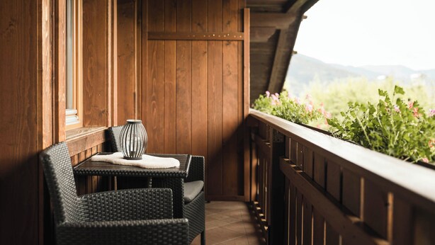 Un balcon en bois, agrémenté de meubles en osier, offrant une vue sur la verdure et les montagnes.