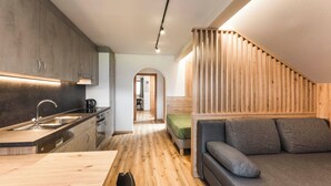 Une cuisine moderne dotée d’un plan de travail en bois et d’appareils électroménagers intégrés, un coin repas avec une table en bois, et un espace salon confortable avec un canapé et des coussins.