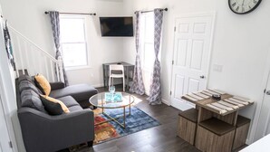 A living room with a gray sofa, a small round coffee table, a TV mounted on the wall, and a wooden side table. - Amazing Beach house  with 2 Units booked together (Ventnor City)