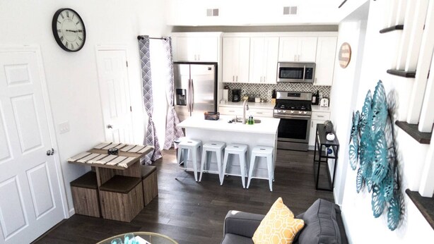 A modern kitchen with white cabinets, a stainless steel refrigerator, and a microwave. There is a dining area with a wooden table and bar stools. - Amazing Beach house  with 2 Units booked together (Ventnor City)