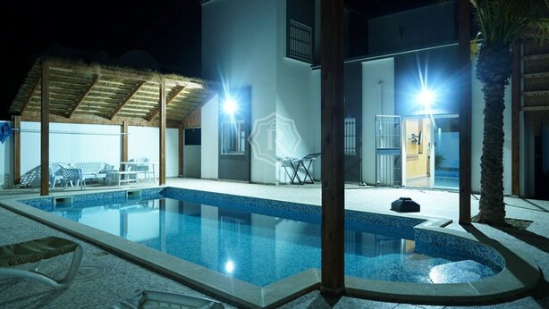A swimming pool with lounge chairs and a covered seating area at night. - Luxurious villa with swimming pool in Midoun (djerba midoun)