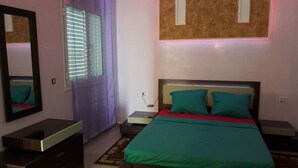 A bedroom with a bed, a nightstand, a mirror, and a window with blinds. - Luxurious villa with swimming pool in Midoun (djerba midoun)