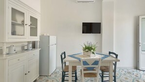 A compact kitchen with white cabinetry, a built-in refrigerator, a dining table with chairs, and a mounted flat-screen TV. - 1688 Villa Blu Cobalto - Appartamento 2 (San Pietro in Bevagna)