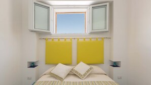 A bedroom with a bed, two yellow headboards, a window above the bed, and a striped bedspread. - 1688 Villa Blu Cobalto - Appartamento 2 (San Pietro in Bevagna)