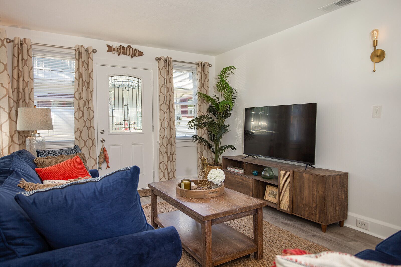 A living room with a blue sofa, a wooden coffee table, a TV on a wooden stand, and a door with a window.