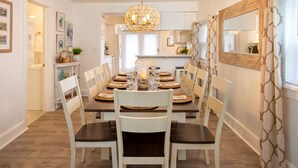 A dining room with a long table set for six, white chairs, and a hanging light fixture.