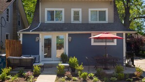 A two-story house with a front porch, a red umbrella, and a small garden.
