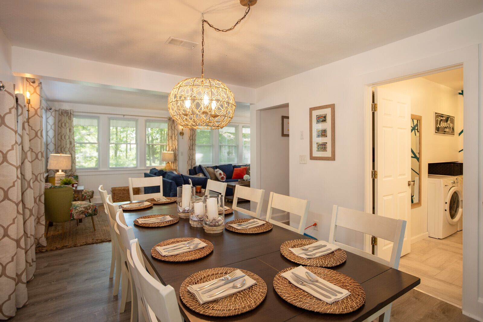 A dining area with a dark wooden table set for six, surrounded by white chairs.