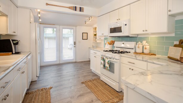 A modern kitchen with white cabinetry, a marble countertop, a gas stove, and a microwave.