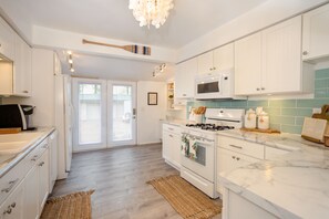 A modern kitchen with white cabinetry, a marble countertop, a gas stove, and a microwave.