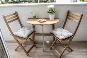 Dos sillas de madera con cojines, una mesita con una planta en maceta, un vaso de bebida verde y un plato con comida.