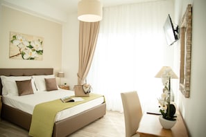 Una habitación de hotel con cama, mesita de noche, lámpara y una planta en maceta.