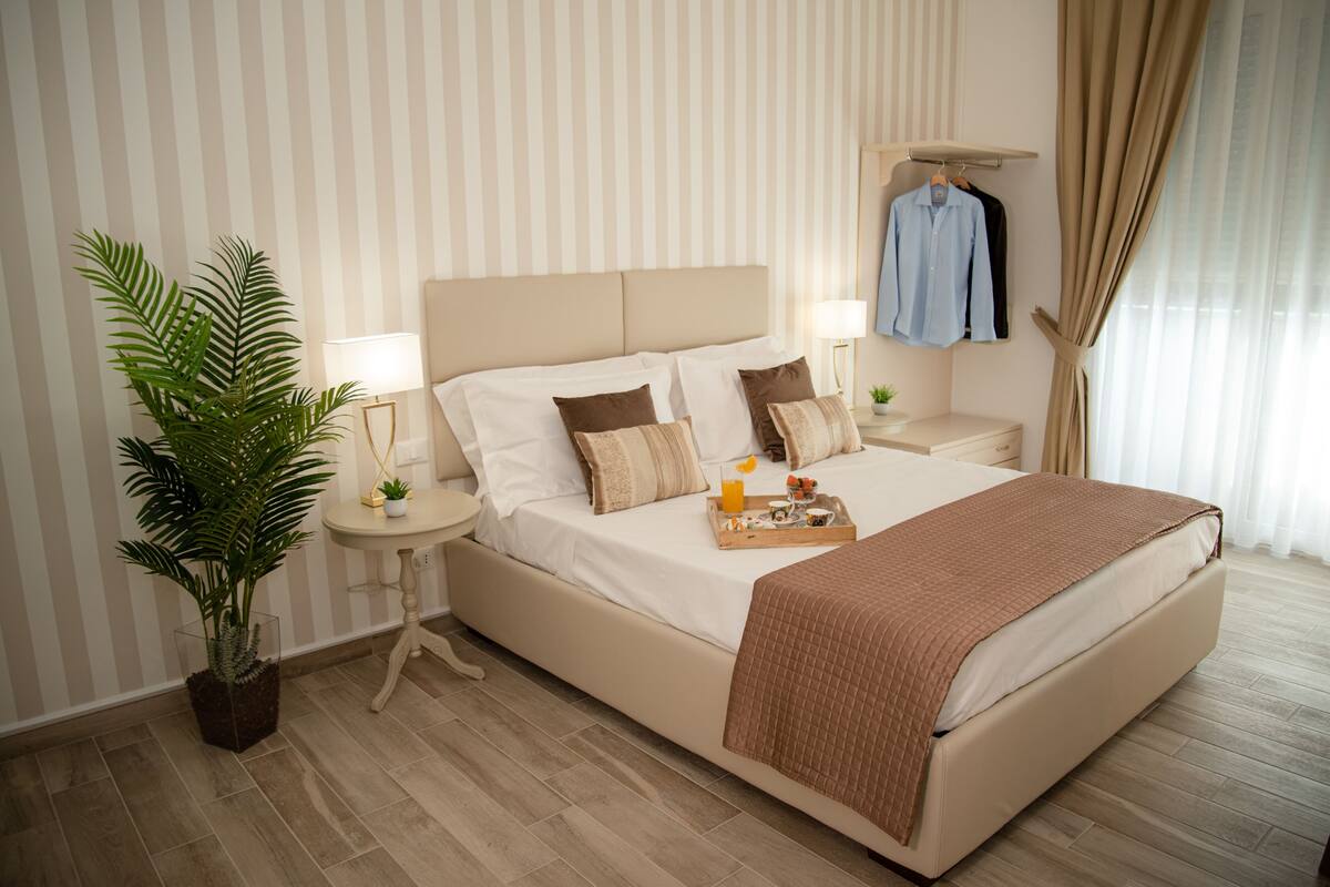 Ein Hotelzimmer mit einem großen Bett, Nachttischen, einer Zimmerpflanze und einer Kleiderstange.