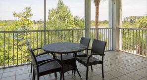 Un balcone con un tavolo rotondo e quattro sedie, affaccia su un paesaggio verde e rigoglioso con alberi e uno specchio d'acqua.