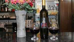 Una botella de vino del Hotel Qeroli, dos copas de vino y un florero con flores sobre una barra.