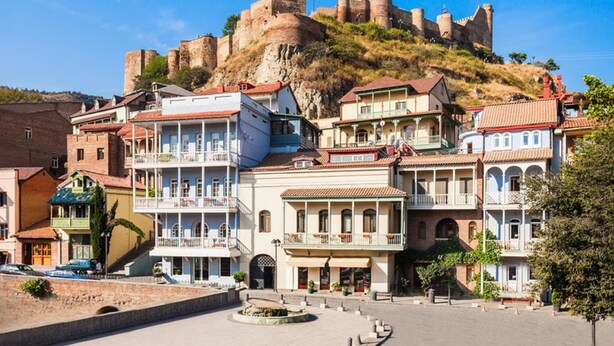 Un pueblo histórico con un castillo destacado en una colina, edificios coloridos y una plaza central.
