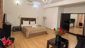 Una habitación de hotel moderna con una cama grande, una zona de estar con sofá y sillones, una mesita y un espejo.