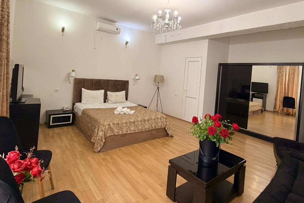 Una habitación de hotel moderna con una cama grande, una zona de estar con sofá y sillones, una mesita y un espejo.