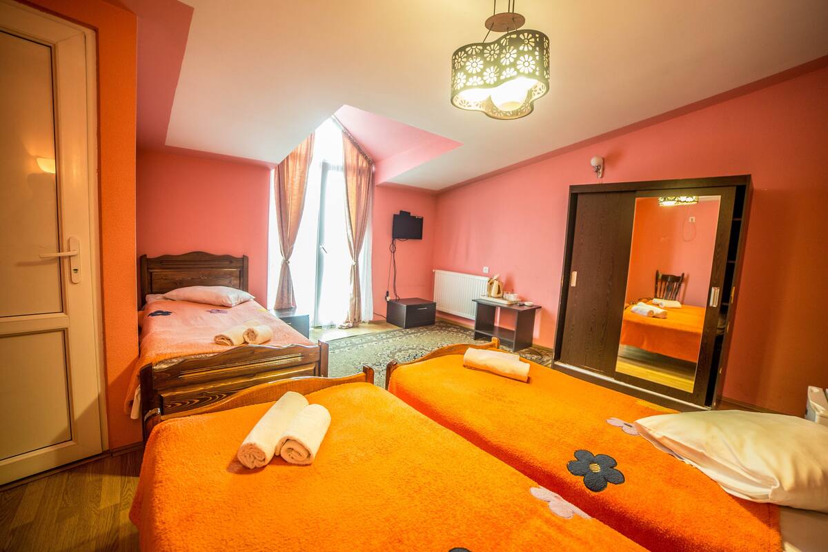 Habitación de hotel con dos camas, un espejo grande, un armario de madera, un escritorio y una ventana con cortinas.