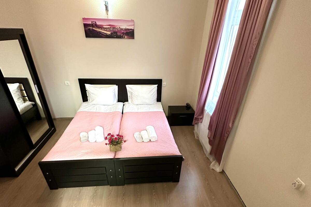 Un dormitorio con una cama grande, una mesita de noche, un espejo y una ventana con cortinas.