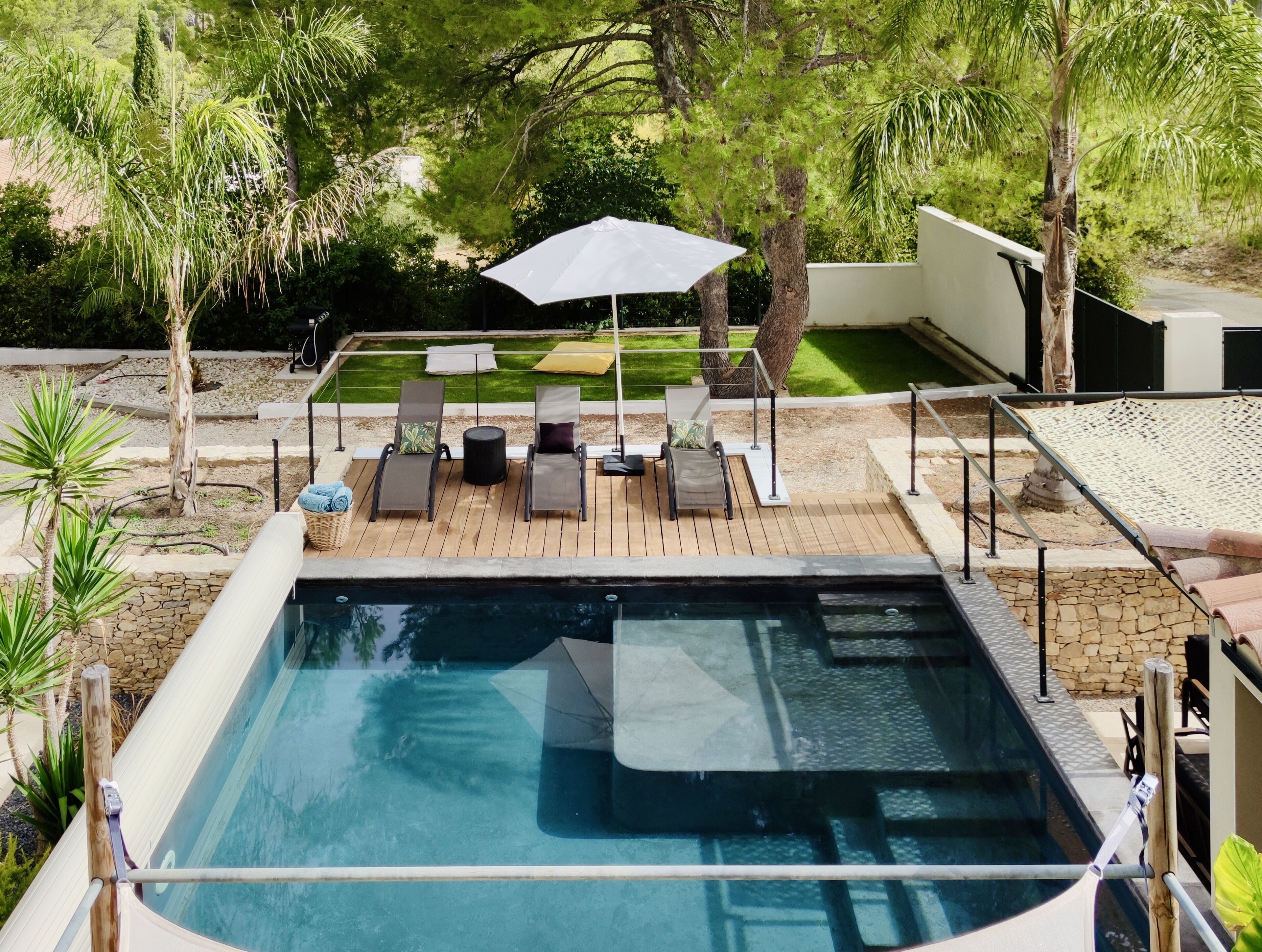 Ein Swimmingpool mit Liegestühlen und Sonnenschirm, umgeben von einem Garten und Bäumen.
