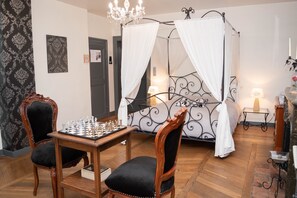 A bedroom with a four-poster bed, a chandelier, a chessboard, and a wooden chair. - La Fée Maison (Châtel-sur-Moselle)