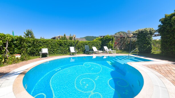 A circular swimming pool with a tiled pattern, surrounded by a brick deck and white lounge chairs. - Villa Stefania (Barano d'Ischia)