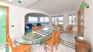 A spacious dining area with a glass-top table, wooden chairs, and a view of the sea. - Villa Stefania (Barano d'Ischia)