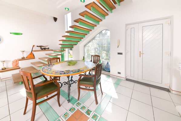 A dining area with a round table, chairs, and a staircase with green steps. - Villa Stefania (Barano d'Ischia)