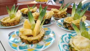 A table with plates of pineapple slices garnished with green leaves and grapes. - Delfina (Lampedusa)