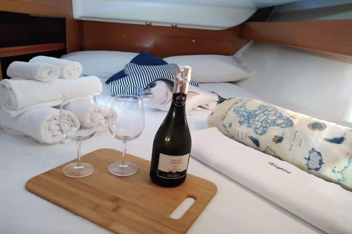 A neatly made bed with rolled towels, a bottle of wine, and two glasses on a wooden tray.